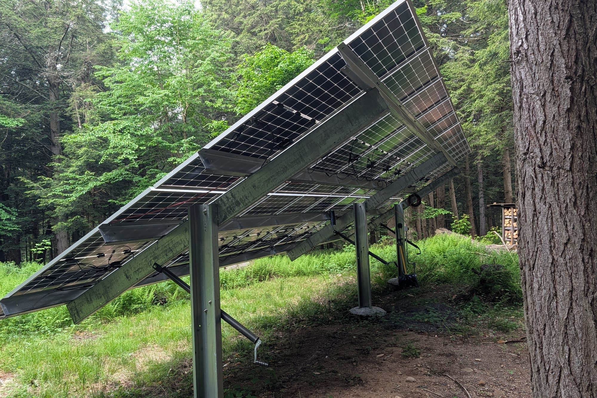 The underside of a bifacial array in the woods, with the hand crank that sets the tilt.